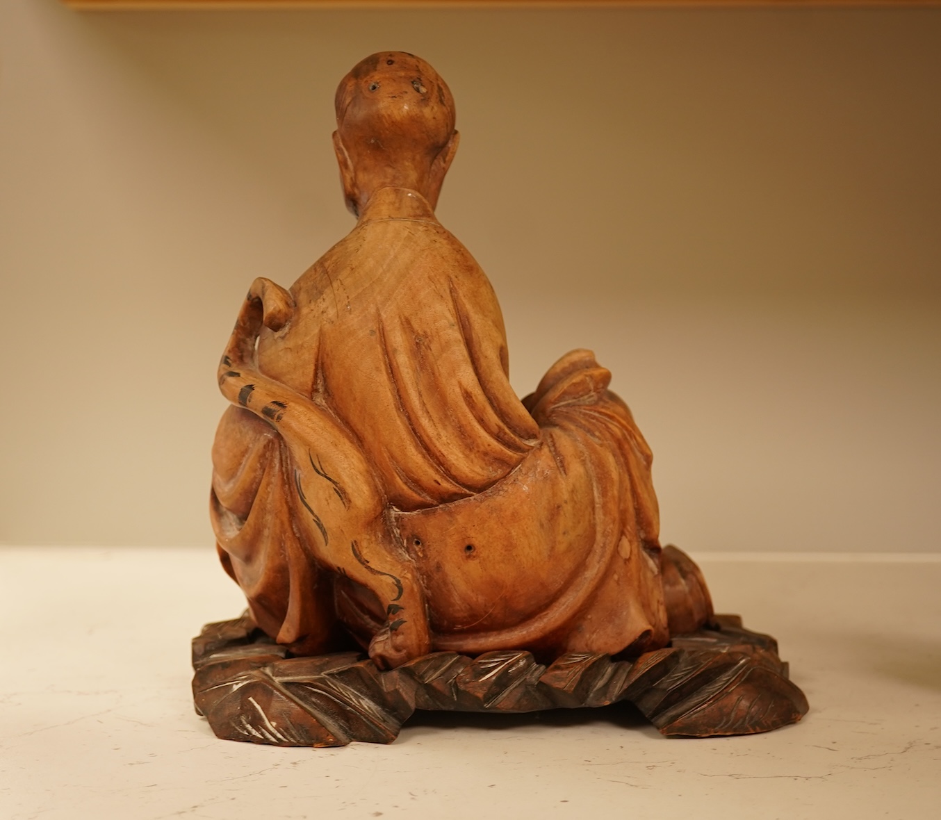 A Chinese hardwood carving of a seated luohan and tiger on hardwood stand, 24cm high including stand.